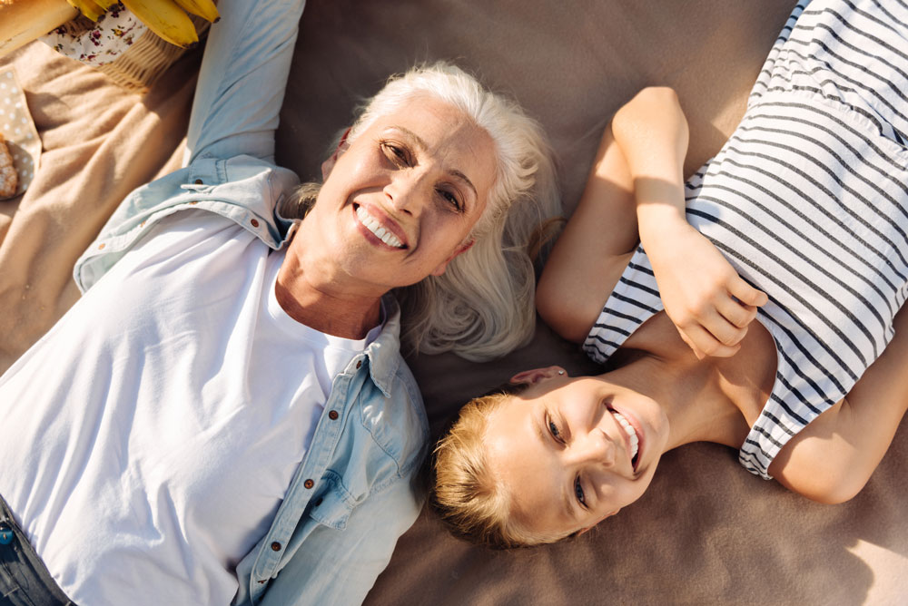 A grandmother and grandaughter laying on blanket with big smiles on their faces